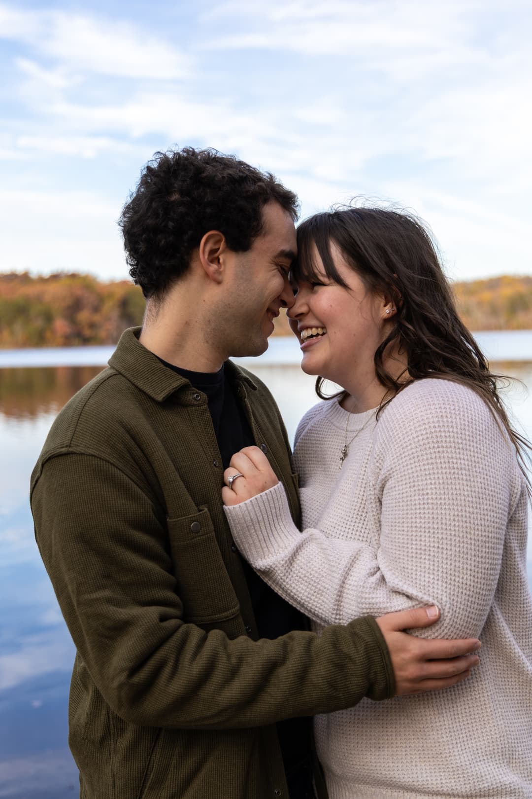 A couple embraces in front of a lake.