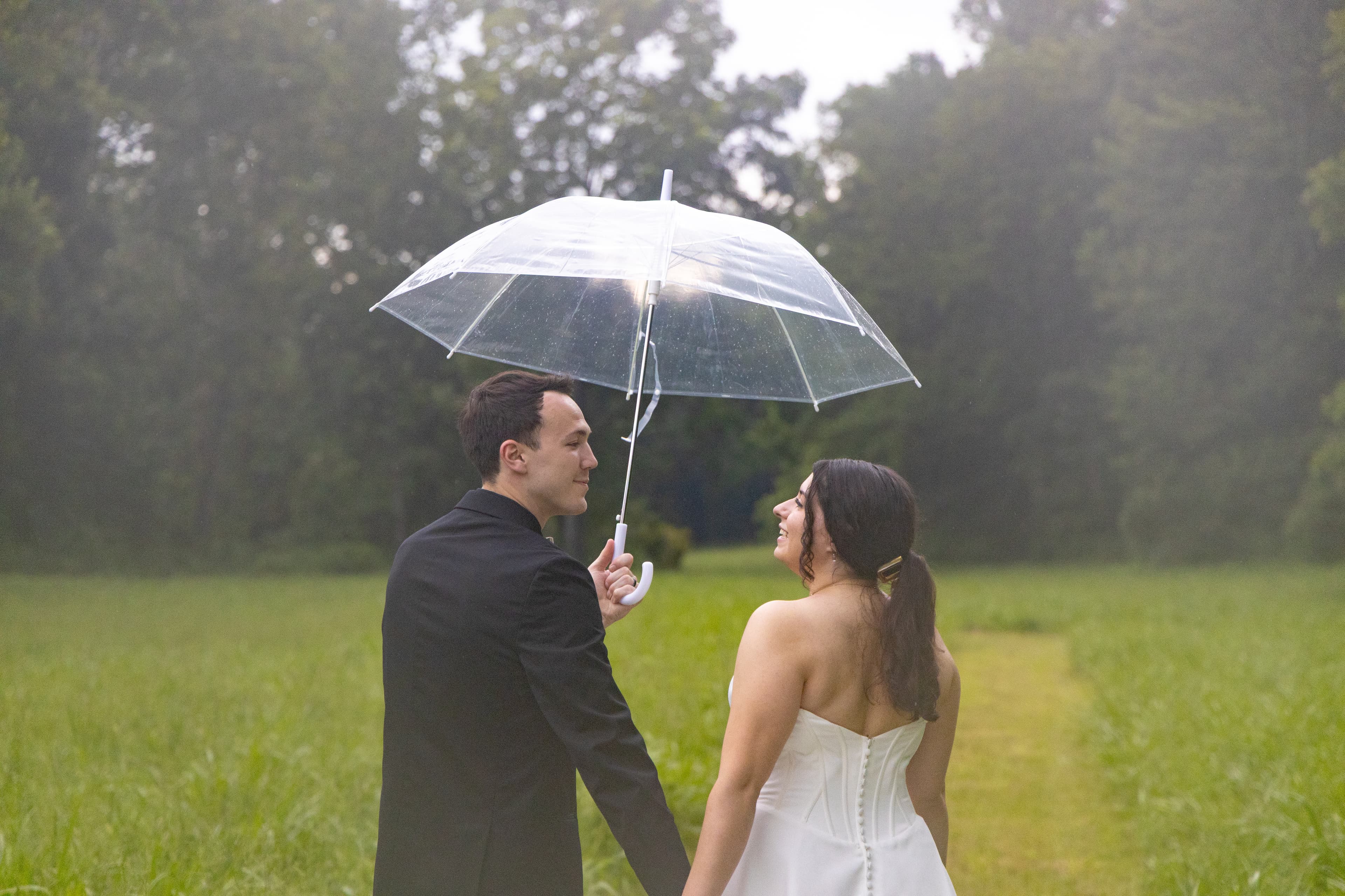 A newly wed couple looks at each other underneath an umbrella.