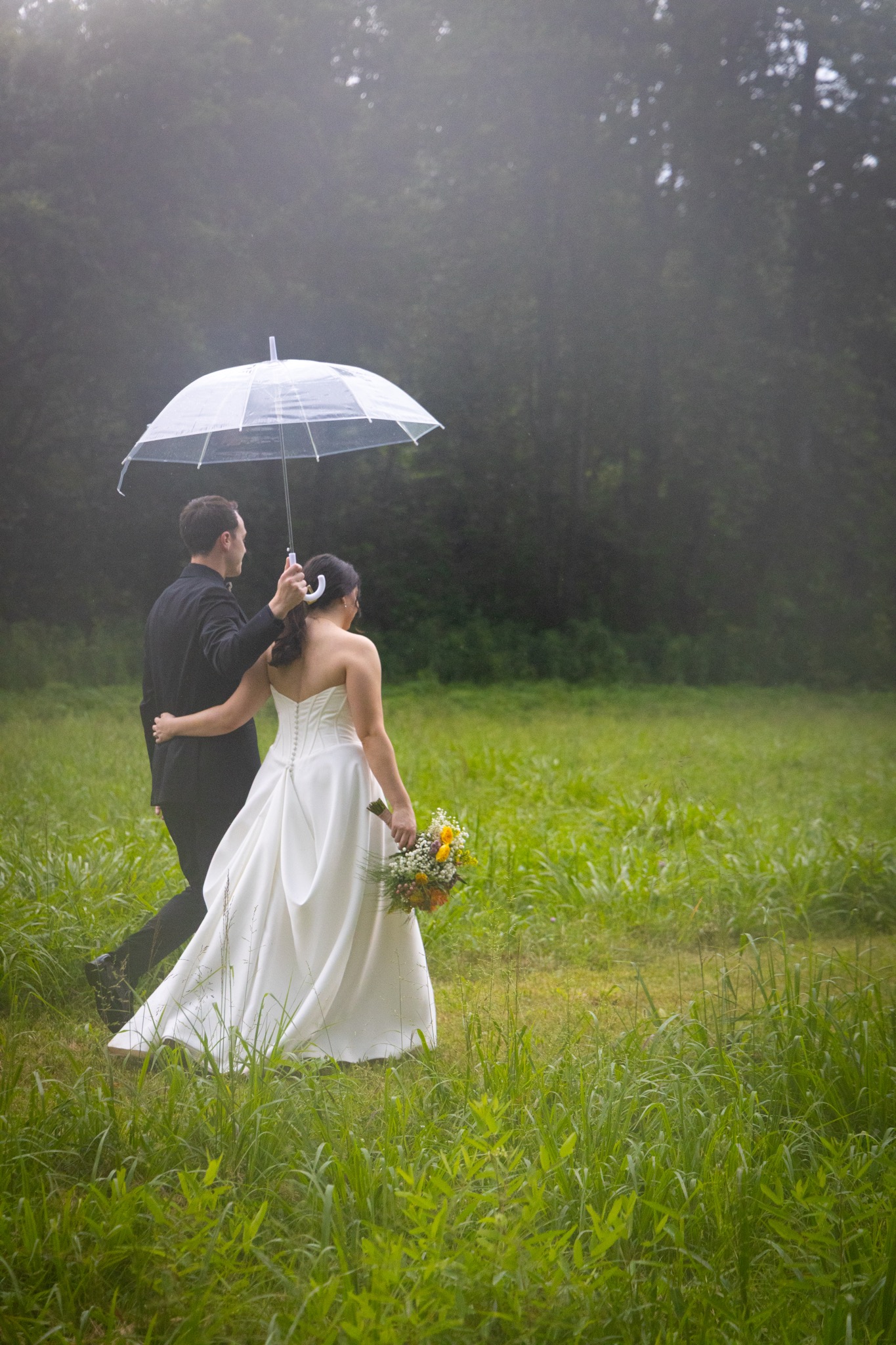 Picture of a married couple sharing an intimate moment in a field with an umbrella.